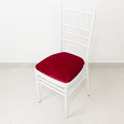 White chiavari chair with red velvet cushion on a plain background