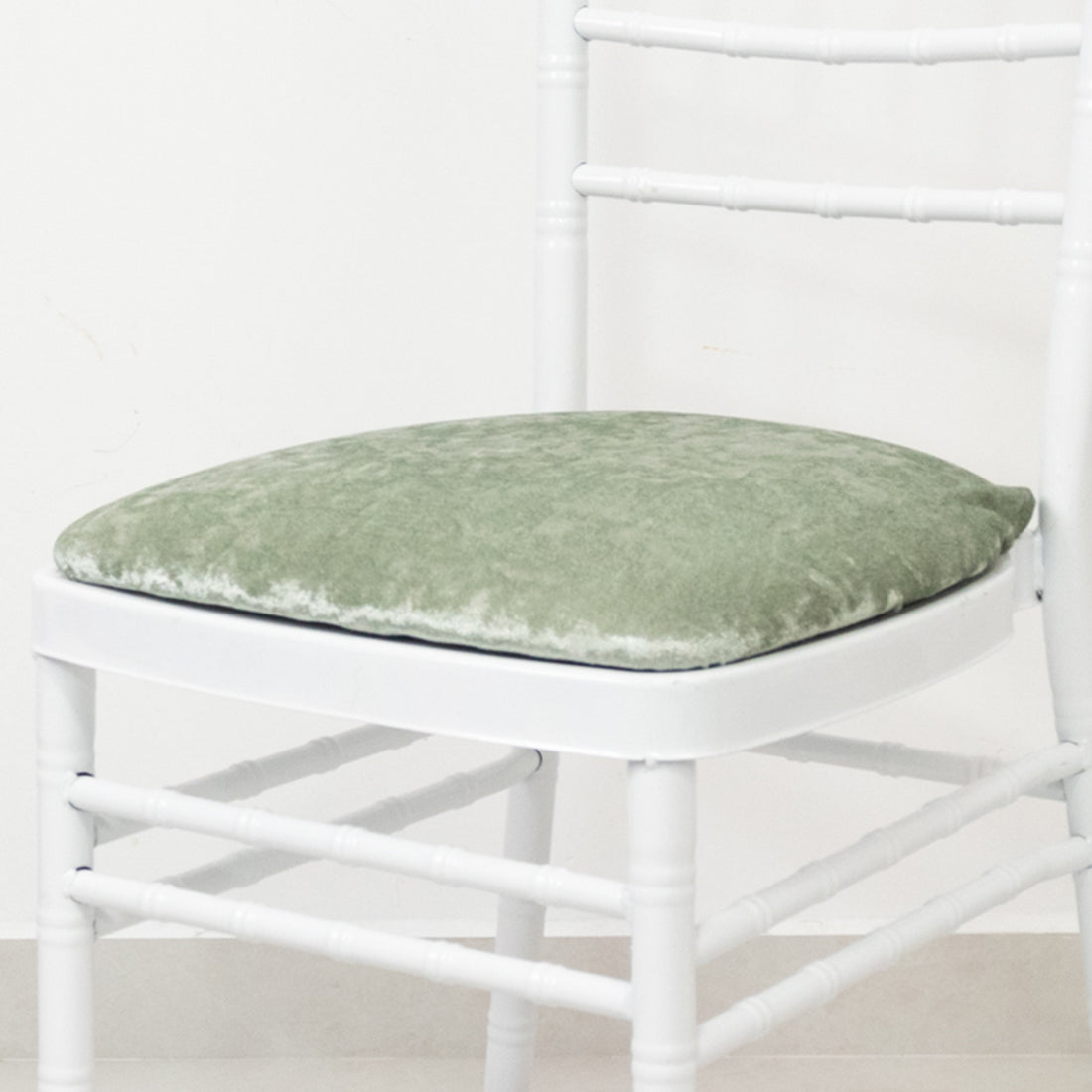 Green velvet chair cushion on a white chair.
