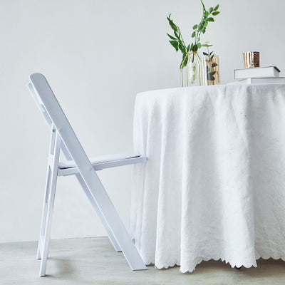 White folding chair beside a round table with a white tablecloth and decorative items.