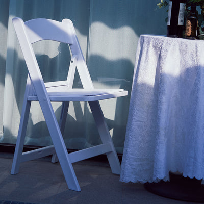 White folding chair beside a table with a lace tablecloth.