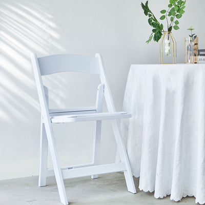 White folding chair beside a table with a decorative vase and a tablecloth.