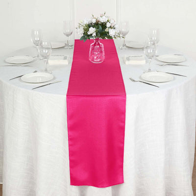 Pink satin table runner on a white table with set dining ware.