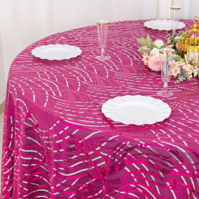 Round pink tablecloth with wavy patterns set for dining with white plates and floral centerpiece.