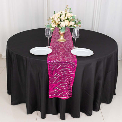 Black round table with a pink table runner, white plates, and floral centerpiece.