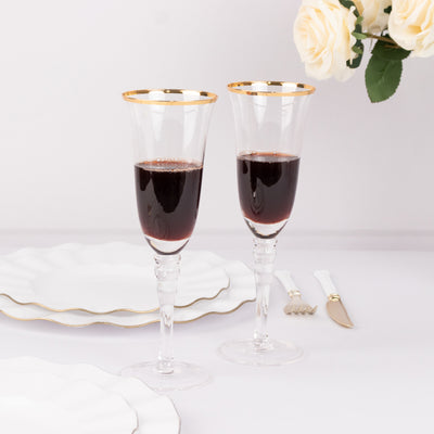Elegant crystal flutes with gold rim, filled with red wine, on a white table setting.