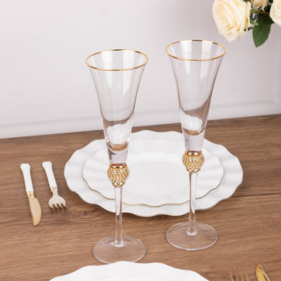 Elegant crystal champagne flutes with gold accents on a wooden table setting.