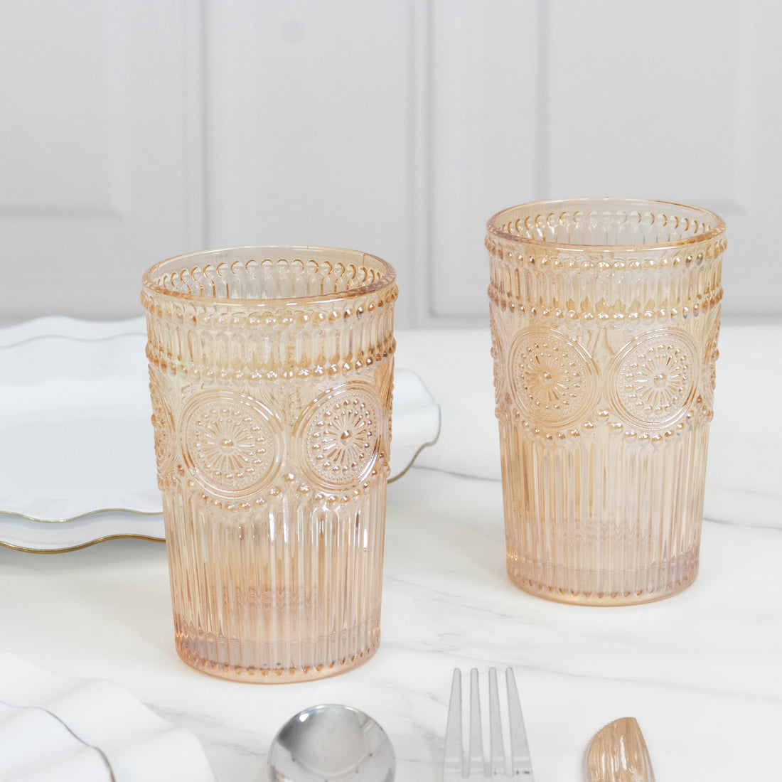 Decorative glass tumblers in soft pink hue on a marble surface.