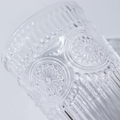 Clear glass tumbler with intricate embossed design details.