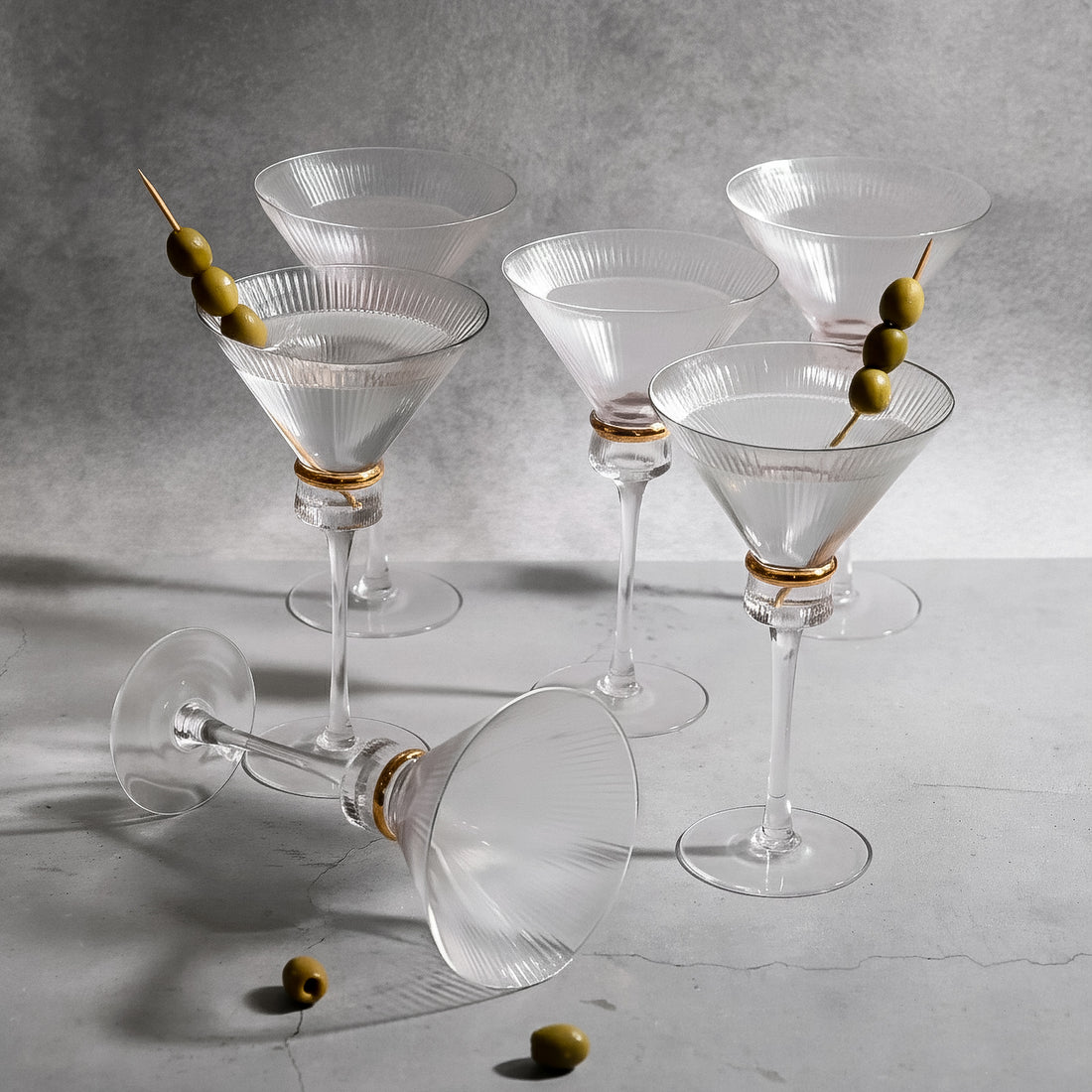 Elegant glass martini glasses with olives on a textured surface.