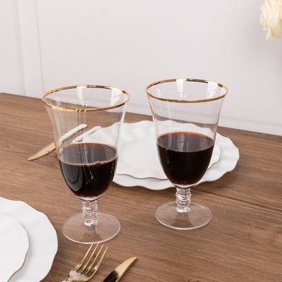 Elegant glass goblets with gold rims filled with red wine on a wooden table.