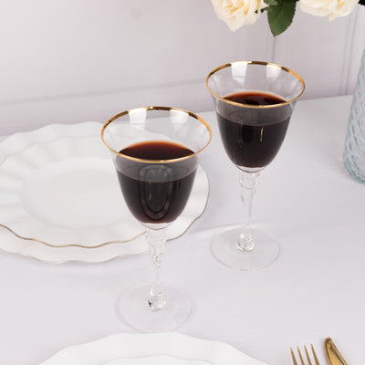 Elegant glass goblets with gold rim, filled with red wine.