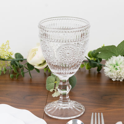 Clear embossed glass goblet on a wooden table with floral accents.