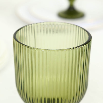 Green ribbed glass tumbler on white background with blurred stemware behind
