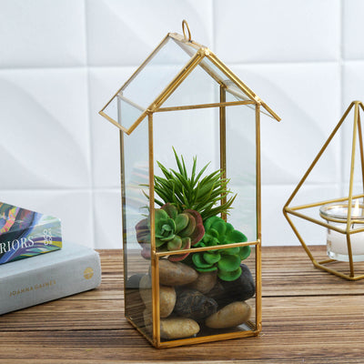 Gold geometric terrarium with succulents and stones on a wooden surface.