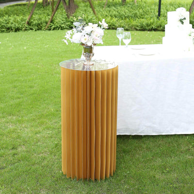 Yellow pleated table with a mirrored top, set outdoors with flowers.