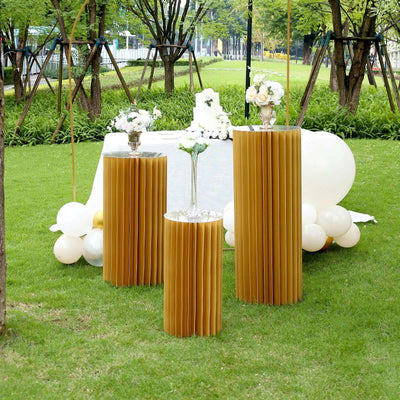 Three elegant gold pleated pedestal tables with floral arrangements in a garden setting.