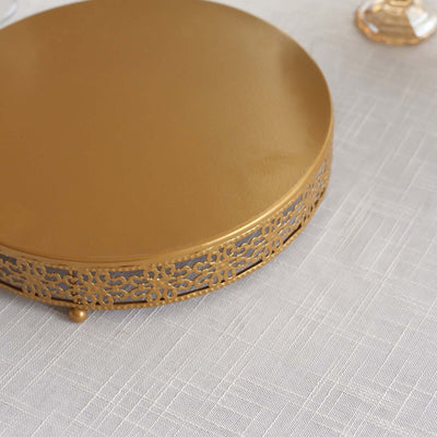 Gold cake stand with intricate lace design on a textured tablecloth.