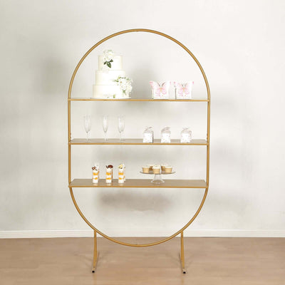 Gold circular display shelf with cakes and glassware against a plain backdrop.