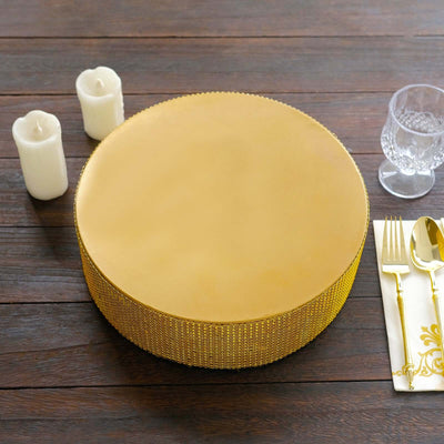 Gold round cake stand on wooden table with candles and silverware.