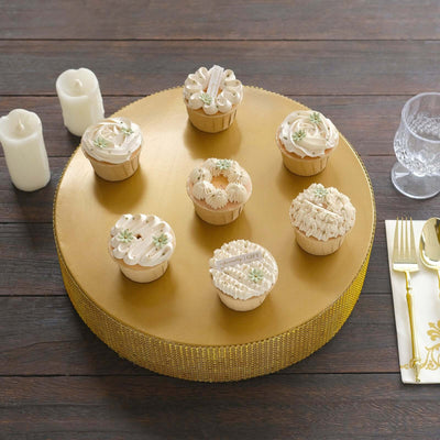 Assorted elegant cupcakes on a gold cake stand with candles and glassware.