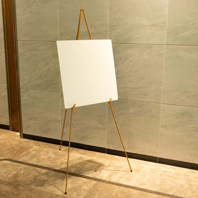 Blank easel board on a gold tripod in a modern interior setting.