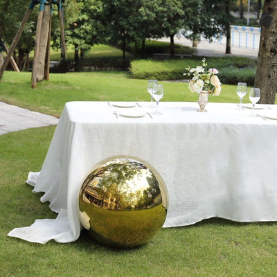 Gold decorative sphere on lawn beside elegantly set outdoor dining table.