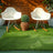 Two modern white rocking chairs on green grass with a potted plant in a wicker basket.