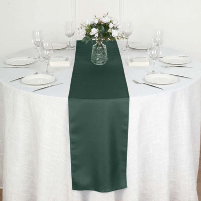 Green table runner on a round table set for dining with glassware and flowers.