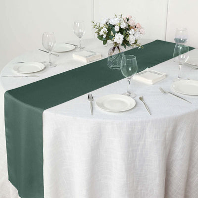 Dark green table runner on a white dining table setting with glassware and flowers.