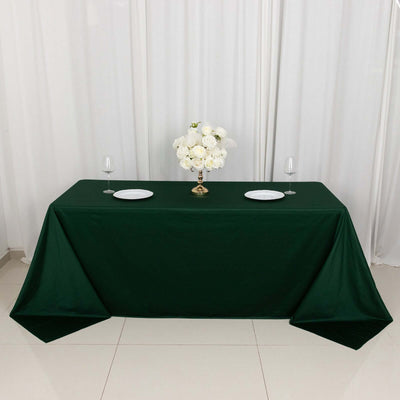 Green tablecloth with white plates and floral centerpiece on a dining table.