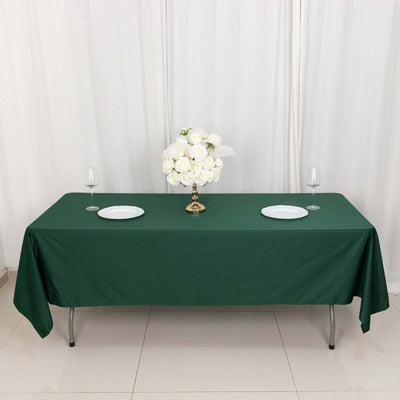 Green tablecloth with white plates and floral centerpiece on a dining table.