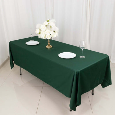 Green tablecloth with white plates and a floral centerpiece on a dining table.