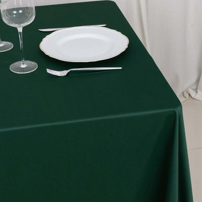 Elegant dark green tablecloth with white plate and glassware.