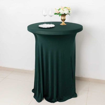 Green round table covered with a fitted tablecloth, styled with glasses and a flower vase.