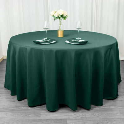 Round dark green tablecloth set with plates and glasses on a dining table.