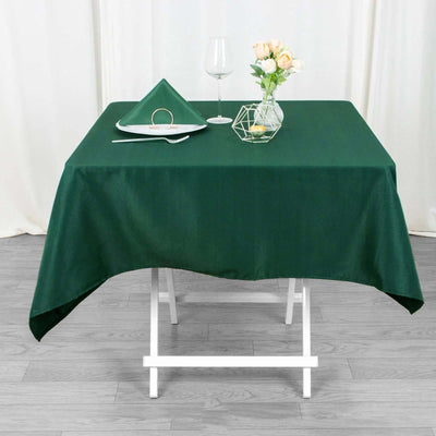 Green tablecloth draped over a table set with a glass, flowers, and napkin.