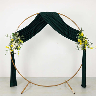 Green draped wedding arch with floral accents on a gold frame.