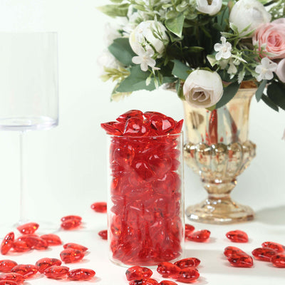 Red heart-shaped candies in a clear jar with flowers in the background.