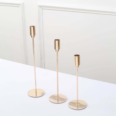 Set of three elegant gold candle holders on a white table.