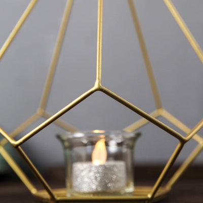 Gold geometric candle holder with a lit tealight inside.