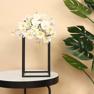 Floral arrangement in a modern black frame on a round table with greenery backdrop.