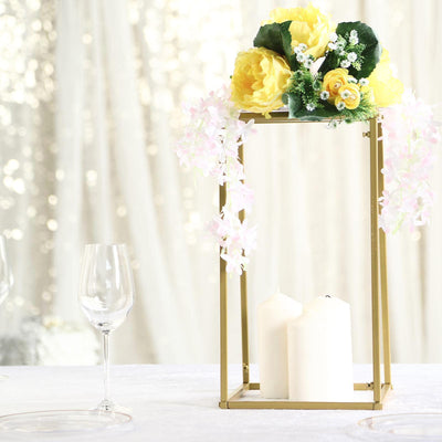 Gold lantern centerpiece with yellow flowers and candles on a table setting.