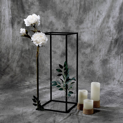 Decorative lantern with faux flowers and candles on textured backdrop.