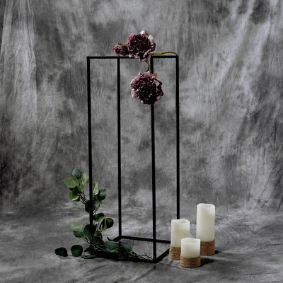 Black geometric flower stand with flowers and candles on a textured gray backdrop.