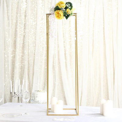 Gold geometric flower stand with yellow roses and candles on a table.