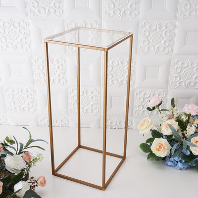 Gold metal display stand with a glass top and floral arrangement.