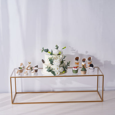 Elegant wedding cake with floral decor and assorted mini desserts on a clear display table.