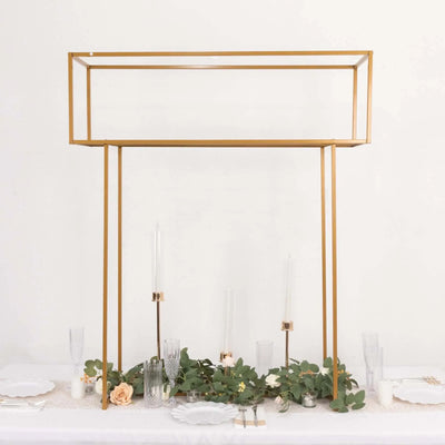 Gold geometric display stand with greenery and candles on a table.