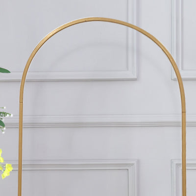Gold arch stand for decor display against a plain backdrop.