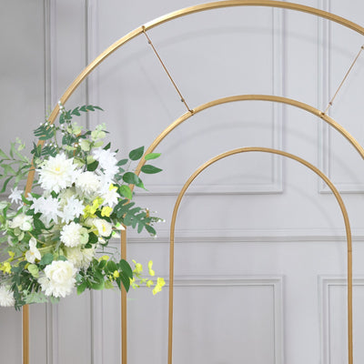 Gold arch with white and yellow floral arrangement, styled against a gray wall.